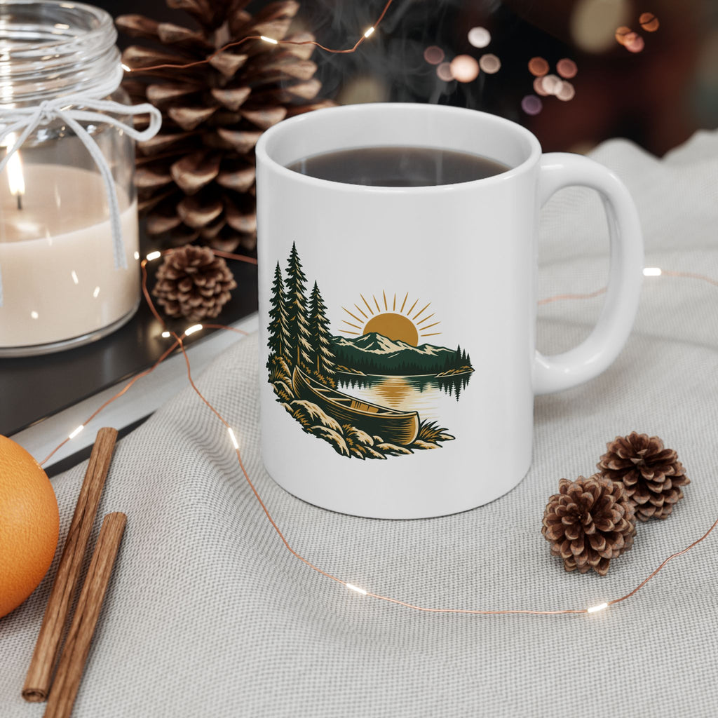 Canoe-and-pines ceramic mug on a table with pinecones and warm drink styling.
