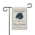 Ivory Welcome to the Lake garden flag with navy lake silhouette and Stay Awhile lettering on a display stand; stand not included.