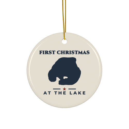 Round ceramic ornament with gold hanging string, navy lake silhouette and “First Christmas at the Lake” lettering on an ivory background.