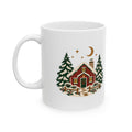 White ceramic mug, handle on the left, with a snowy red cabin, pine trees and crescent moon.